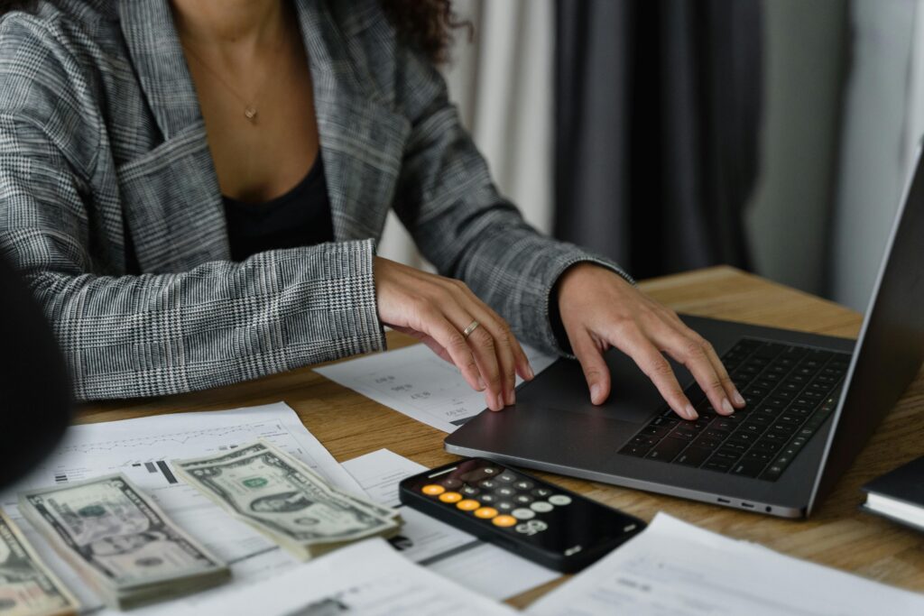 A lady working on her finances with her computer, calculator and few dollar bills with some paperwork