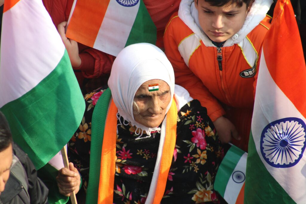 Old Indian woman with forehead painted on with an Indian flag surrounded by other indian people with flag in rally involving indian politics